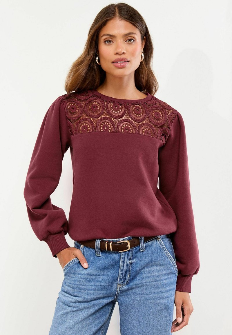 Bordo sweatshirt z čipkastim delom, dolgi rokavi in ribbani manšeti. V kombinaciji z modrimi kavbojkami z visokim pasom in rjavim pasom.