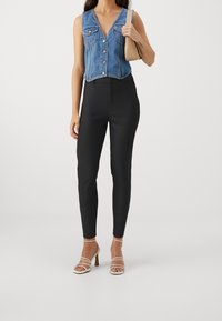 Jeansärmlös topp med knäppning framtill, två bröstfickor; matchad med figurnära svarta byxor och remmar i vitt. Släta texturer, modern stil.