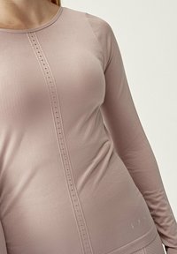 Långärmad topp i mjuk rosa tyg med rund halsringning och knapppanel nedtill. Har en slät textur och en figurnära design.