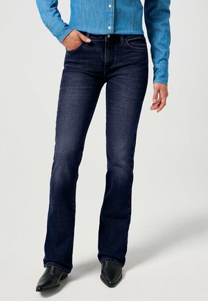 Dark blue denim jeans with a fitted design, slight flare at the bottom, and front pockets. Paired with a light blue button-up shirt.