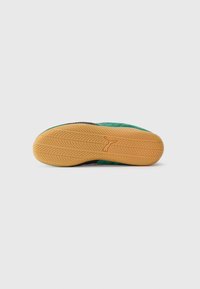 Shoe sole with tan rubber tread featuring a Puma logo, partially visible black and green upper against a plain white background.