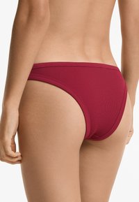 Burgundy ribbat bikiniunderdel med låg midja och slät textur, med en högskuren benöppning. Ingen synlig hårdvara eller detaljer.