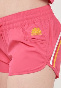 Costumini da bagno rosa con vita elastica, una piccola tasca laterale e strisce a contrasto in bianco e giallo. Logo ricamato in giallo.