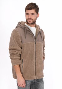 Chaqueta de forro polar marrón con un panel gris y capucha. Cuenta con cierre de cremallera, bolsillos laterales y tejido texturizado. Ajuste informal.