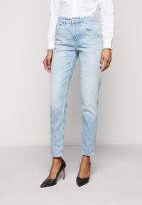 Light blue denim jeans with a straight leg design, subtle fading, front pockets, and a metal button closure, paired with black pointed heels.