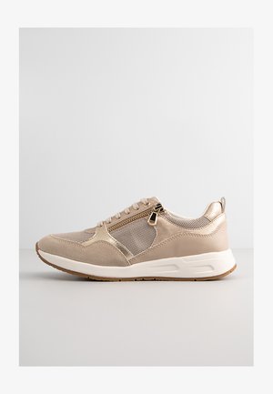 Zapatillas deportivas beige con paneles de malla, acentos de cuero liso, un detalle con cremallera en el lateral y una suela blanca acolchada.