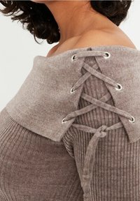 Pull marron côtelé avec un large col épaules dénudées, orné de détails à lacets avec œillets métalliques et tissu doux et texturé.