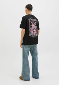 Sort bomulds t-shirt med et pink grafisk design af planter på ryggen, rund hals og afslappet pasform, parret med lyse denim jeans.