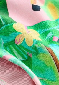 Gros plan sur un tissu plié avec un imprimé coloré de feuilles tropicales et de fleurs jaunes sur fond rose.