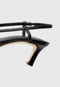 Schwarze, geschnallte High-Heelsandale mit glänzendem Finish, quadratischer Zehenform, dünnen Riemen und schlankem Stiletto-Absatz.