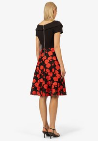 Schwarzes schulterfreies Kleid mit tailliertem Oberteil, ausgestelltem Rock und rotem Blumenmuster. Verfügt über einen Reißverschluss auf der Rückseite und eine geschichtete Textur.
