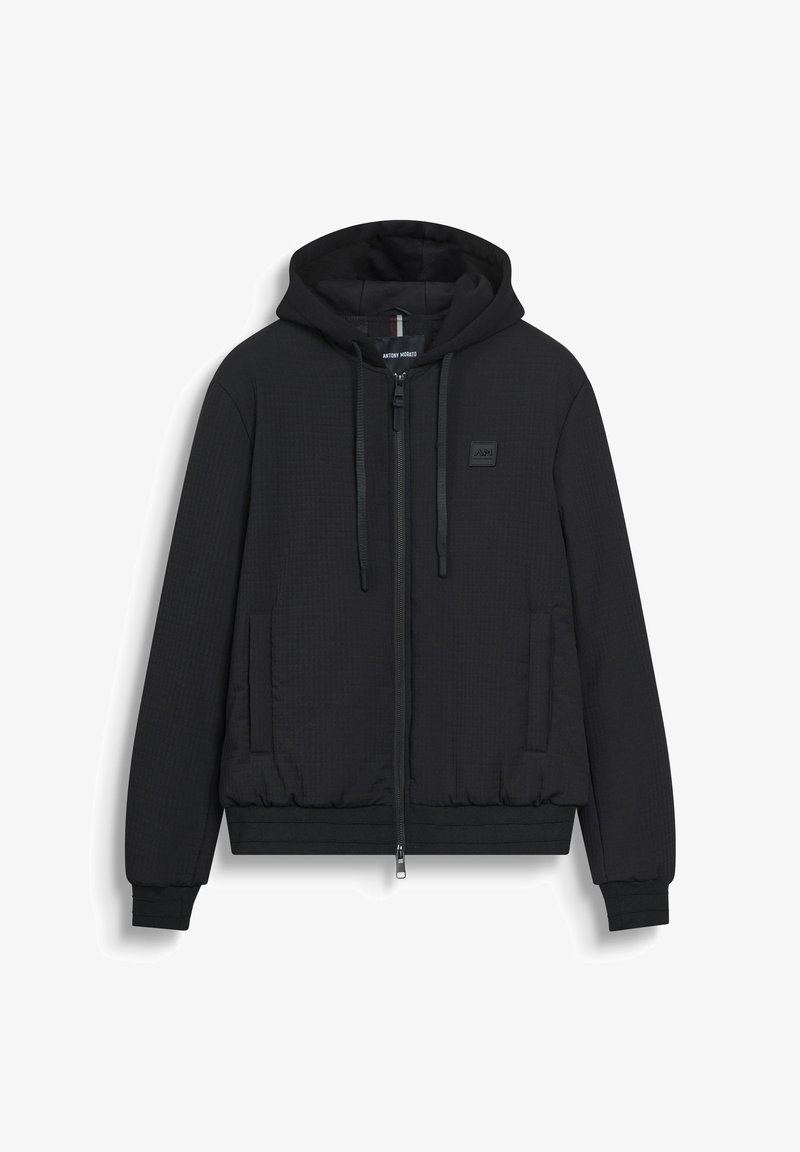 Felpa nera trapuntata con zip, dotata di tasche anteriori, cappuccio regolabile con corde, polsini e vita a coste, caratterizzata da una piccola etichetta con logo sul petto.