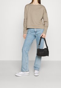 Sweat-shirt court beige, jean évasé bleu clair, baskets blanches avec accents argent és, et un petit sac à main noir avec une bandoulière.