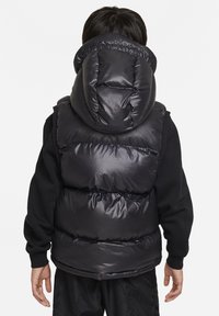 Chaleco acolchado negro con un alto cuello, gran capucha y diseño acolchado. Textura suave y brillante con acolchado en varias capas. Las características clave incluyen un cierre frontal con cremallera y puños elásticos.