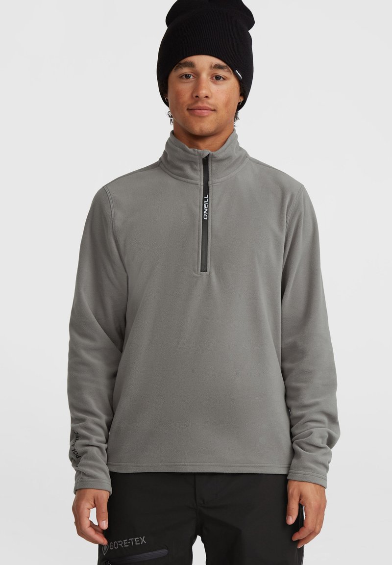 Grijze fleece pullover met een halflange rits, zachte textuur, hoge kraag en logodetail. Draagt met zwarte broek met een GORE-TEX-label.