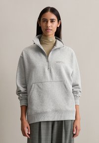 Graue Zip-Hoodie mit Stehkragen, ausgestattet mit einer Fronttasche und "MOTD" Stickerei. Weicher Baumwollmischstoff, lässige Passform, gerippte Bündchen.