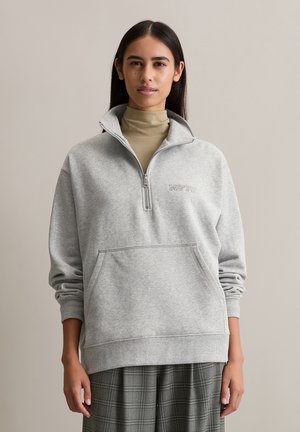 Grijze zip-up sweater met staande kraag, voorzien van een voorzak en "MOTD" borduursel. Zachte katoenmix stof, relaxte pasvorm, ribgebreide manchetten.