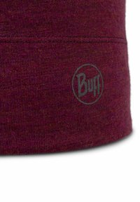 Close-up of maroon knitted fabric with a stitched seam and a small circular Buff logo printed near the bottom edge.