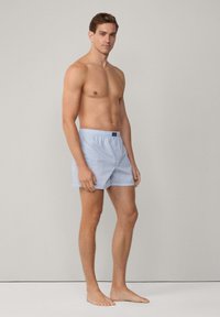 Blå rutiga kalsonger med elastisk midja och knappstängning, tillverkade av lätt bomullstyg, visade på en modell.