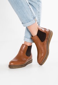 Brown leather ankle boots with elastic side panels and textured rubber soles, featuring a rounded toe and subtle stitching detail.