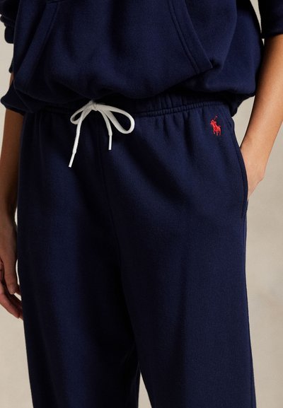 Σκούρο μπλε φόρμα από μαλακό ύφασμα με λευκό κορδόνι και μικρή κόκκινη λεπτομέρεια λογότυπου στην αριστερή πλευρά. Διαθέτει πλαϊνές τσέπες και ελαστική μέση.