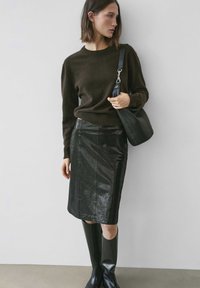 Brauner Strickpullover kombiniert mit einem schwarzen Bleistiftrock aus Lackleder. Accessoires umfassen eine strukturierte schwarze Schultertasche und kniehohe schwarze Stiefel.