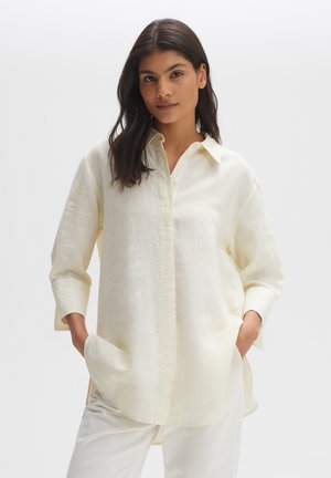 White linen button-up shirt with a relaxed fit, long sleeves, and side pockets. Features a classic collar and light texture.