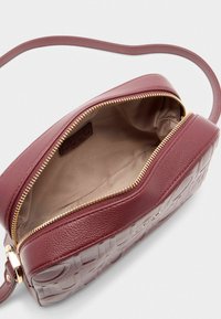 Borsa a tracolla in pelle bordeaux con superficie texture e zip dorata. L'interno è foderato con un tessuto beige morbido.