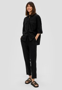 Czarna lniana koszula z dwiema kieszeniami z przodu, luźny krój i krótkie rękawy. Połączona z czarnymi lnianymi spodniami i czarnymi sandałami na paski.