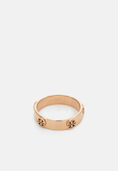 Gold-tone metal ring with a smooth band, featuring three decorative circular accents, each with a cut-out logo pattern.