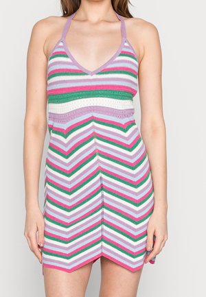 Femme portant une robe sans manches à col halter avec des rayures en chevron et horizontales rose, verte, blanche et lavande, avec un décolleté en V.