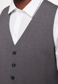 Szary kamizelka z teksturowanej tkaniny, z dekoltem w serek i trzema czarnymi guzikami z przodu, w połączeniu z białą koszulą z kołnierzykiem.