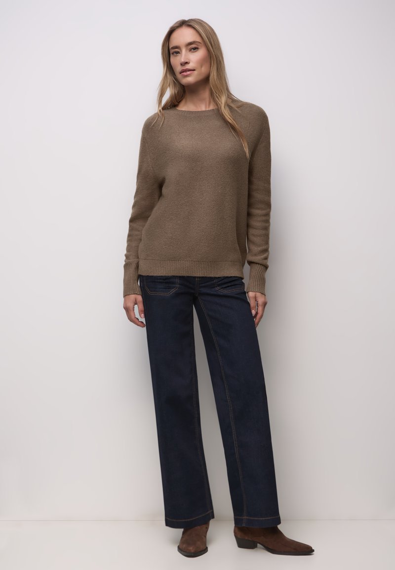 Pull tricot marron clair avec ourlet côtelé, associé à un jean large bleu foncé avec des coutures contrastées. Des bottines marron complètent le look.