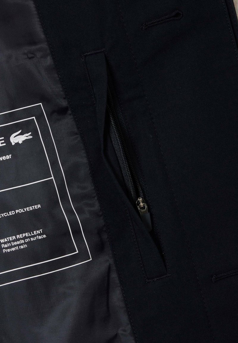 Interior de chaqueta negra fabricado en poliéster reciclado, con un bolsillo con cremallera, recubrimiento repelente al agua y etiqueta de instrucciones de cuidado.