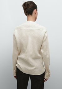 Langærmet skjorte i lys beige linned med et enkelt design, der har en let tekstur, knapmanchetter og en buet fald bagpå.