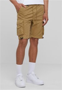Khakifärgade cargoshorts med flera sidofickor, dragsko i midjan och justerbar fåll, tillverkade av slitstarkt tyg. Bärs med vita strumpor och sneakers.
