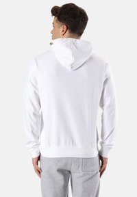 Sudadera blanca con capucha y textura suave, con capucha ajustable y puños de canalé. Combinada con pantalones de chándal gris claro.