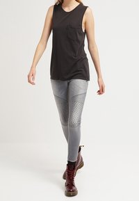 Top negro sin mangas con un bolsillo en el pecho, combinado con pantalones vaqueros ajustados de color gris claro que presentan un diseño acolchado. Botines burdeos con cordones.