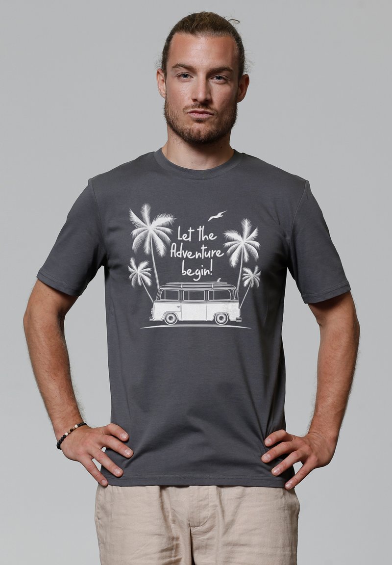 T-shirt en coton gris avec un imprimé graphique blanc d'une van, de palmiers, et le texte « Que l'aventure commence ! » sur un fond neutre.