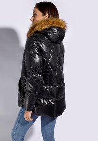 Giacca a vento nera con finitura lucida, cappuccio foderato in pelliccia e design trapuntato. Presenta tasche laterali e una silhouette aderente.