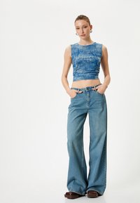 Niebieski skórzany crop top z teksturowanym wzorem w połączeniu z jeansami w kolorze niebieskim o wysokim stanie i szerokich nogawkach. Brązowe buty na platformie dopełniają całość.