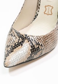 Escarpin à bout pointu en simili cuir texturé façon peau de serpent aux nuances de noir, beige et blanc, avec une finition brillante et un logo intérieur discret.