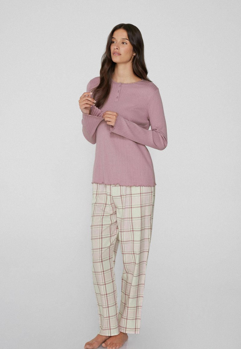 Top de manga larga de color púrpura claro y con canalé, con un escote redondo y detalles de botones, combinado con pantalones de cuadros crema que presentan líneas rosas y grises.