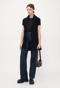 Svart strikket ermeløs cardigan, tettsittende t-skjorte, høytlivte mørke denim jeans, kraftige svarte platåsko og en liten bordeaux farget håndveske.