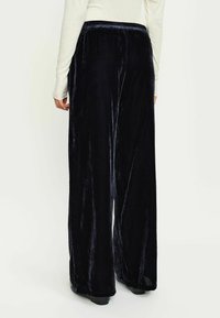 Pantaloni a gamba larga in velluto blu scuro con una texture morbida, dotati di una vita elastica e di una silhouette fluida e ampia.