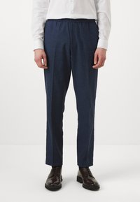 Mornarsko modri hlače z elastičnim pasom in ravnim krojem, narejene iz strukturirane tkanine, v kombinaciji s rjavimi poslovnimi čevlji.