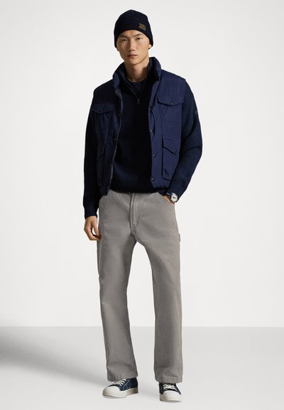 Laivaston tikkitakki tumma villapaidan päällä, harmaat housut ja siniset lenkkarit. Takkissa on useita taskuja ja kuvioitu neulospinta.