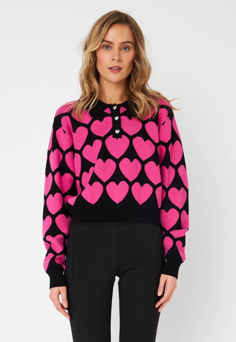 Motivi a cuore rosa su un maglione nero lavorato a maglia. Presenta un collo a camicia con tre bottoni decorativi e maniche lunghe. Silhouette aderente.