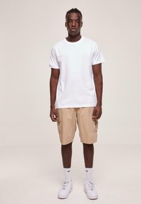 T-shirt en coton blanc, shorts cargo beiges, baskets blanches avec des accents noirs. Design simple, coupe décontractée et poches visibles sur les shorts.