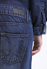 Jeans de mezclilla azul oscuro con un parche visible etiquetado como "LTB", un bolsillo trasero con un sutil detalle de costura y herrajes metálicos plateados.